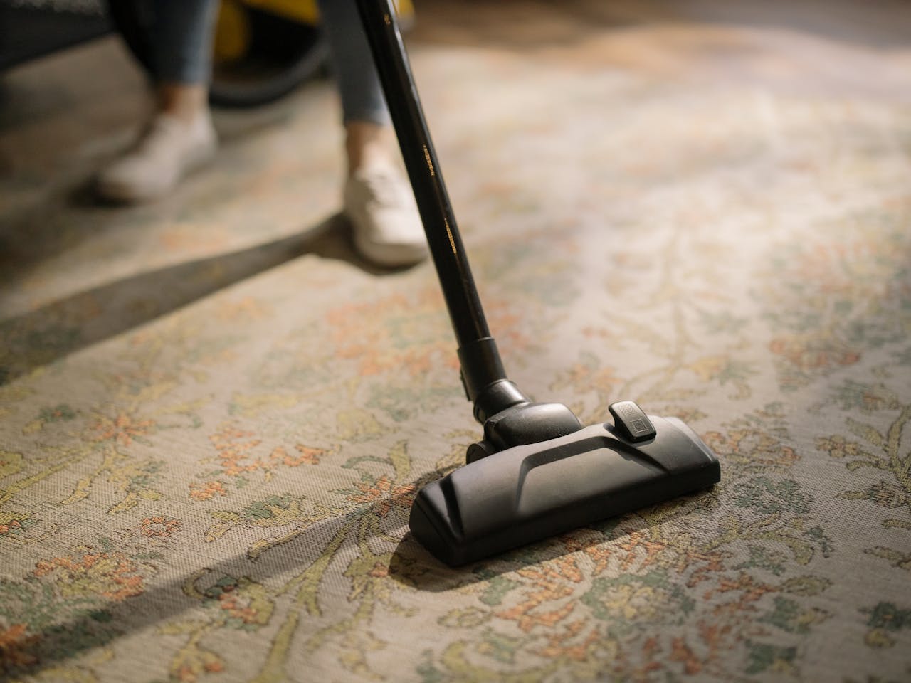 hero-img Close-up of a vacuum cleaner on a patterned carpet in a sunlit room, capturing a moment of household cleaning.